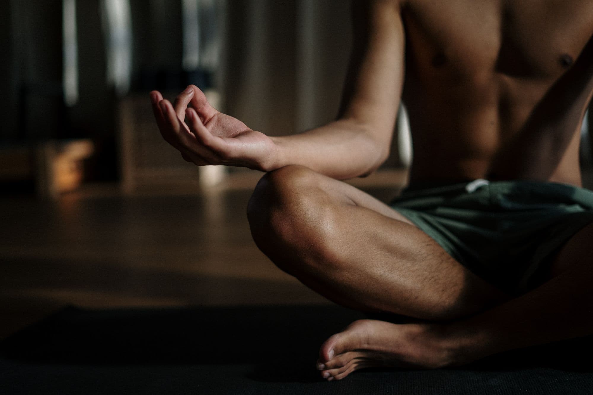 Man in black shorts meditating cross-legged on floor