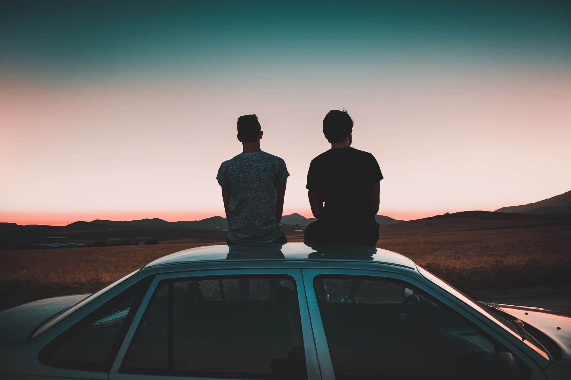 Two young men on car hood watch sunrise