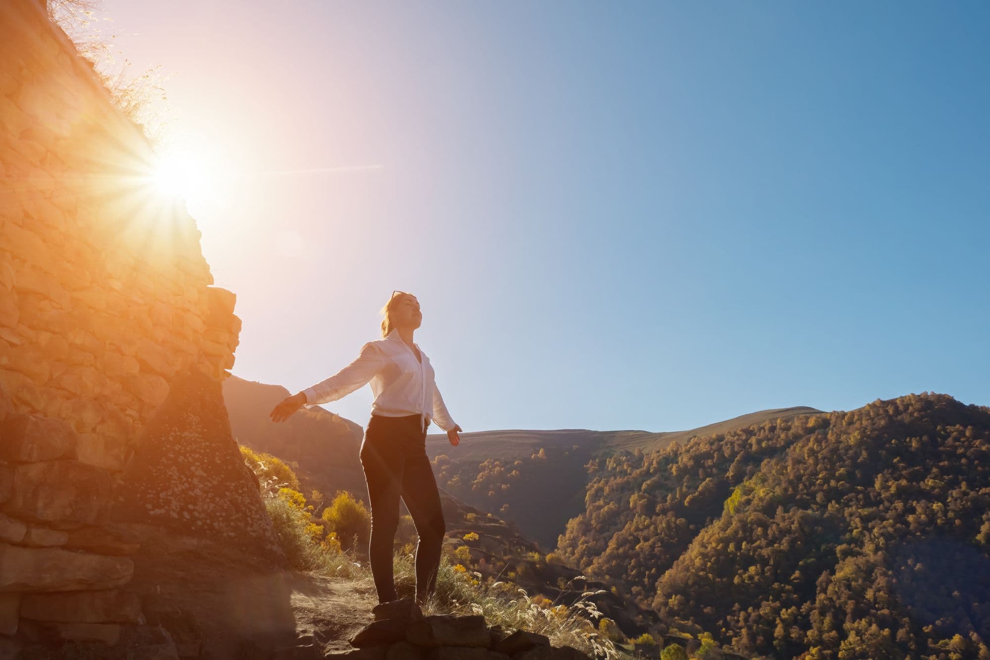 Young woman stands on hill top against mountainous forests