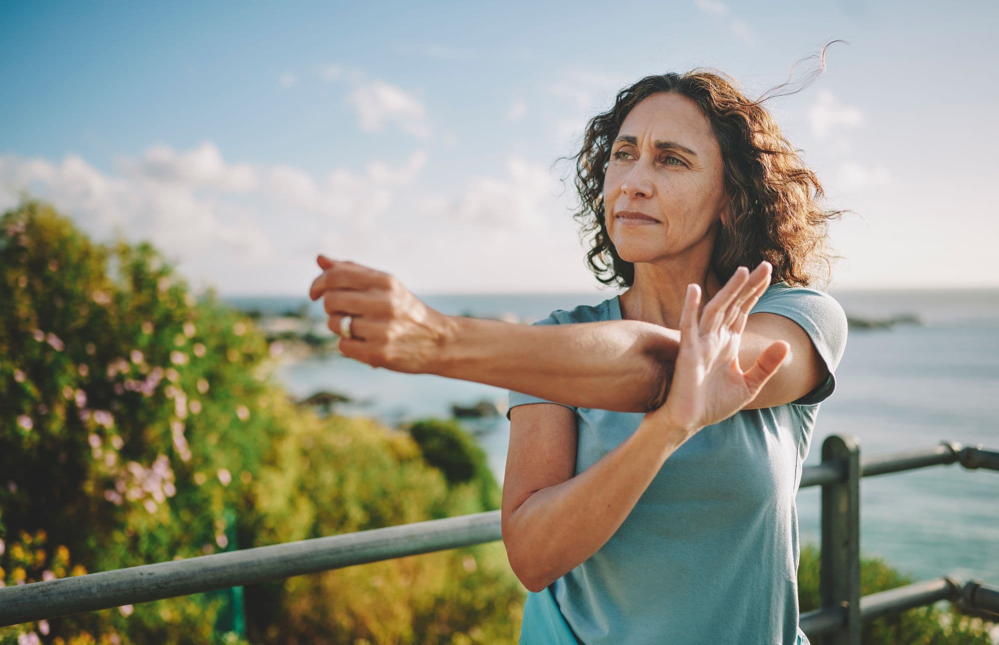 Fit mature woman stretching her arms before a run by the sea